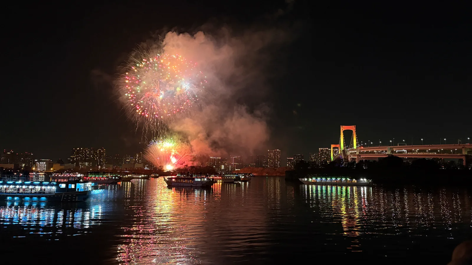 以彩虹大橋與屋形船為背景、在東京灣升空的煙火